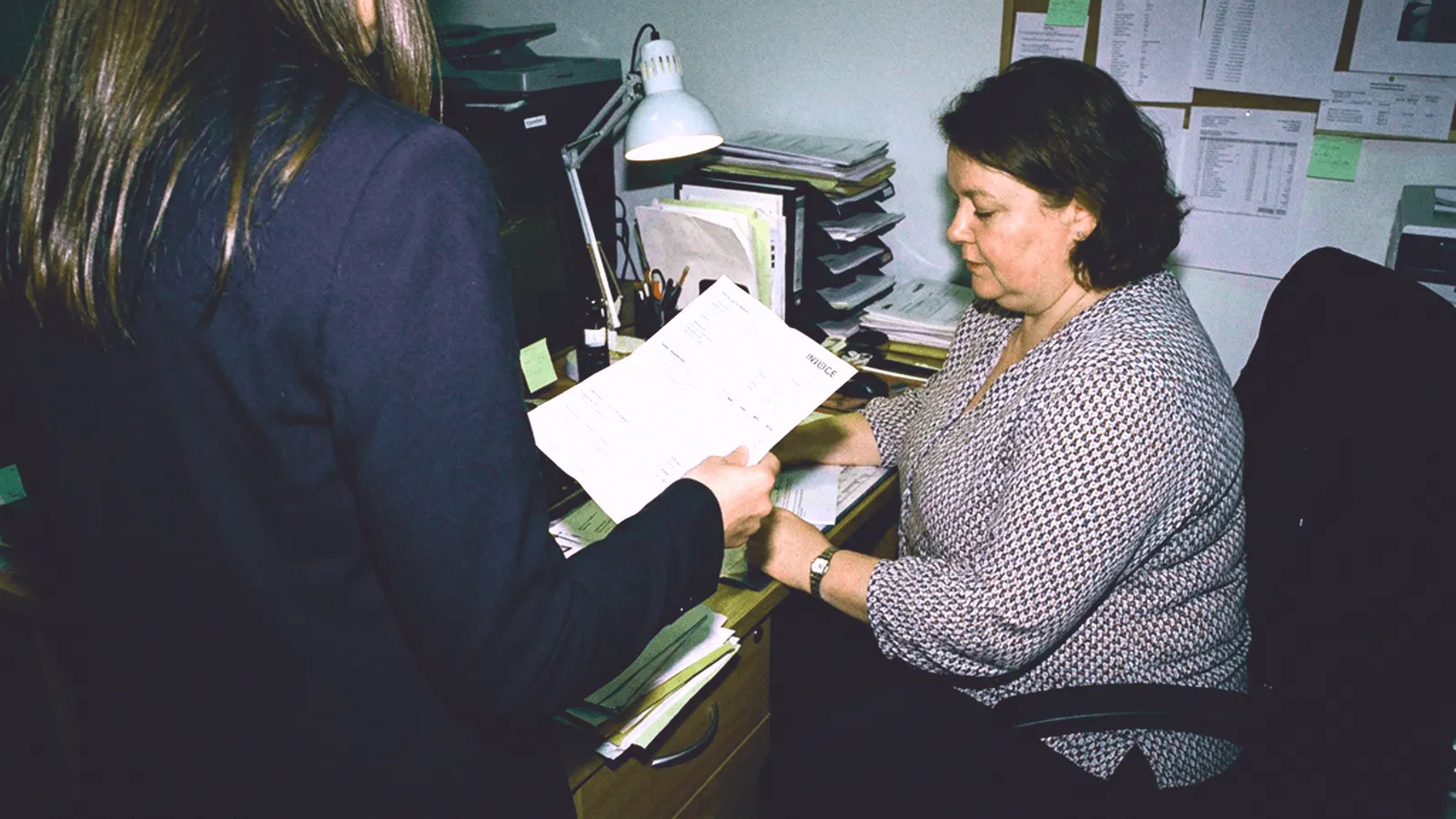 Person handing an unexpected invoice to a woman at an office desk
